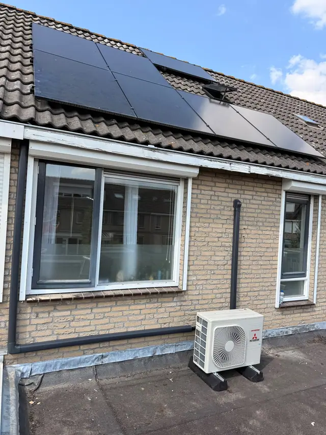 Airco-buitenunit op een plat dak, met zonnepanelen op het schuine dak erboven