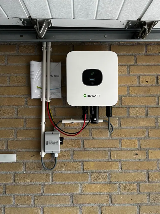 Omvormer aan de buitenmuur onder een carport, met de bekabeling netjes in goten