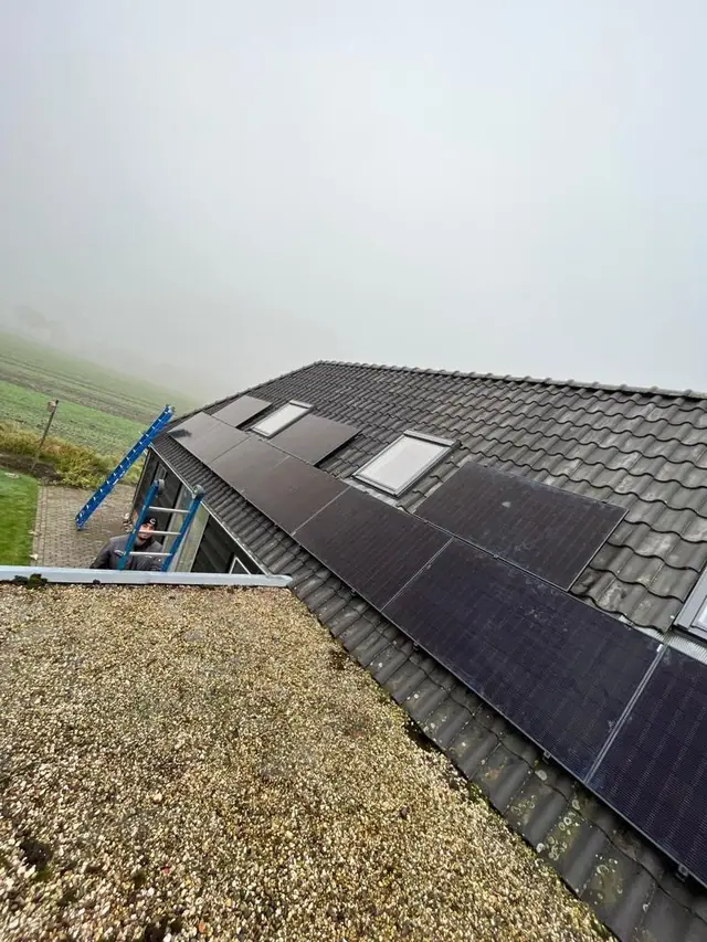 Zwarte zonnepanelen op een pannendak met uitzicht over de polder