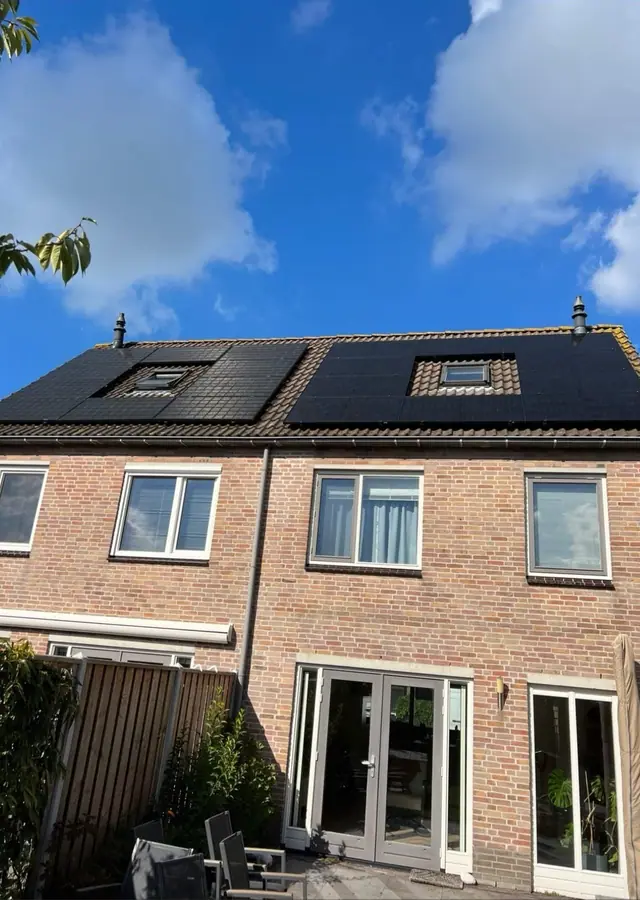Achterkant van een tussenwoning met zwarte zonnepanelen rond de dakkapel