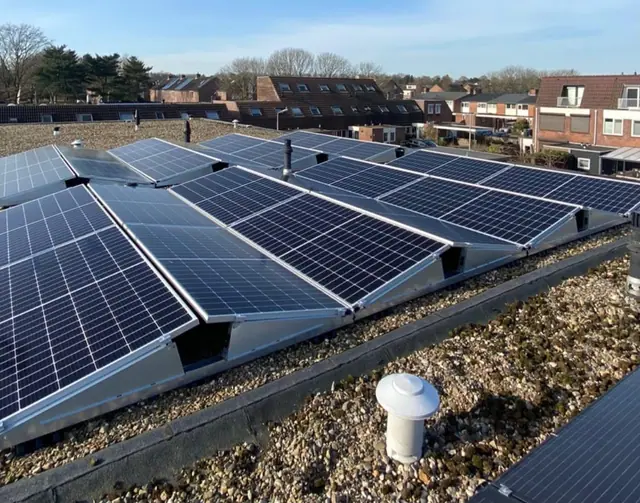 Plat dak met rijen zonnepanelen boven een woonwijk