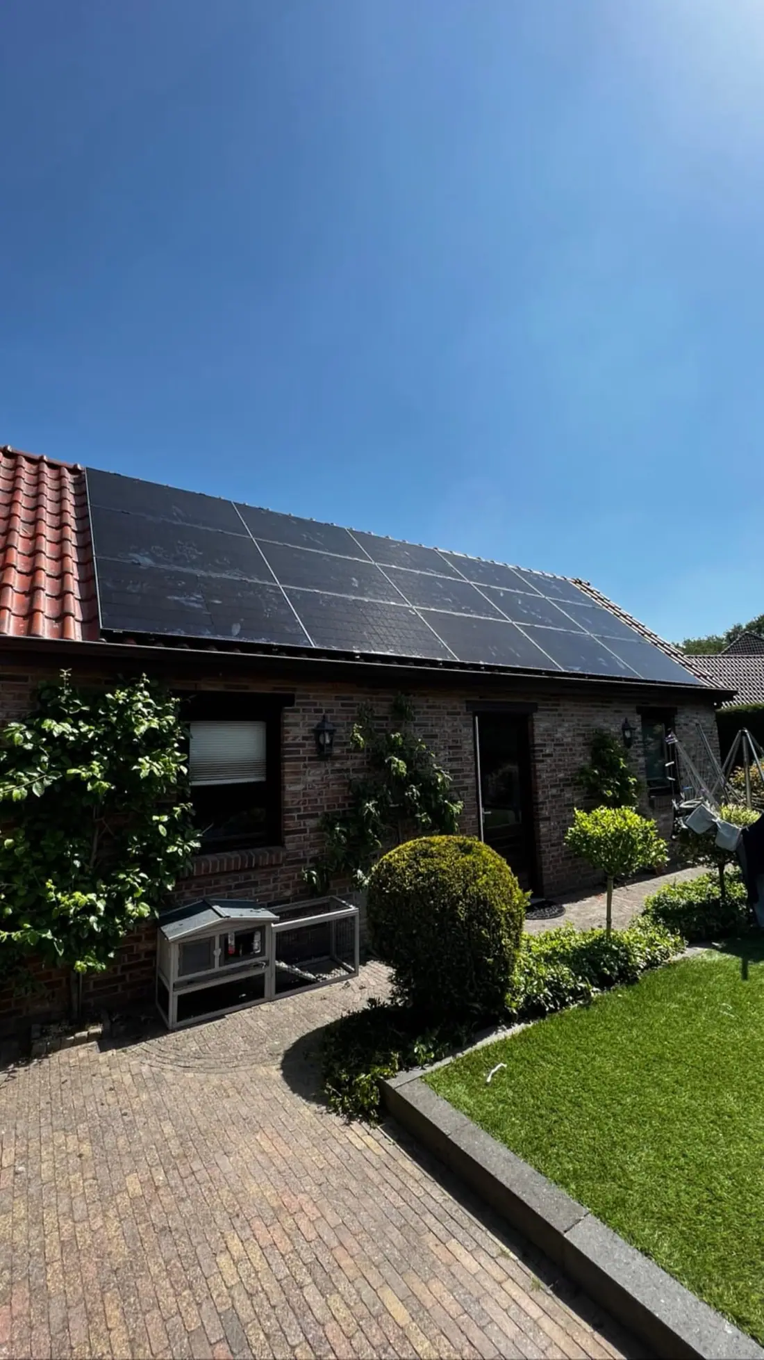 Woning met zwarte zonnepanelen op het pannendak, met de voortuin op de voorgrond
