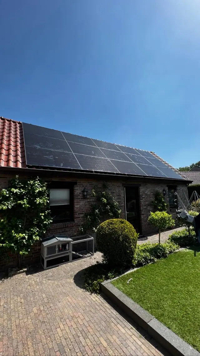Woning met zwarte zonnepanelen op het pannendak, met de voortuin op de voorgrond